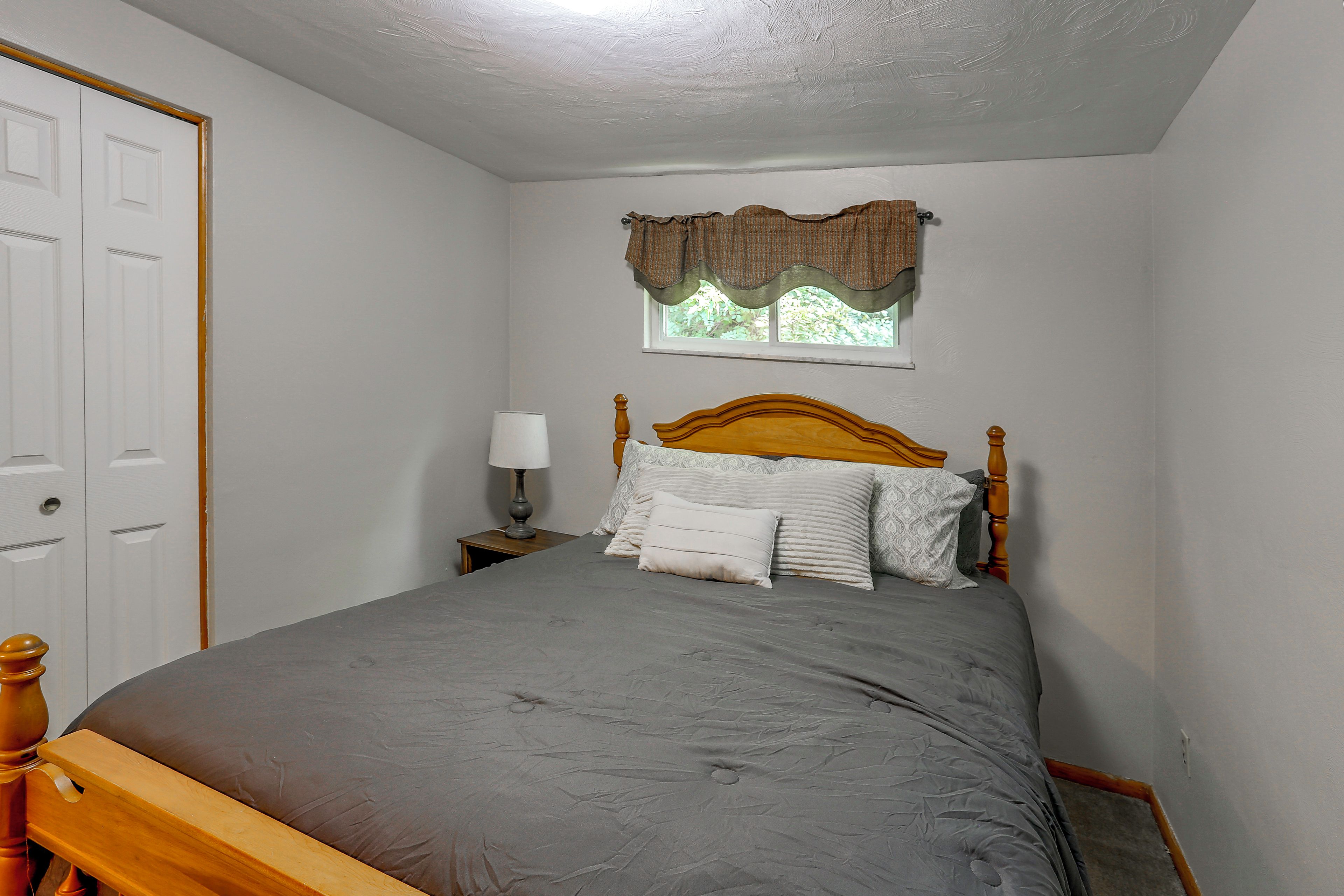 Un dormitorio con una cama individual, una mesita de noche, una lámpara, una ventana con cortinero y una puerta.