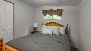 Un dormitorio con una cama individual, una mesita de noche, una lámpara, una ventana con cortinero y una puerta.