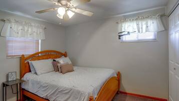 A bedroom with a wooden bed, a ceiling fan, and two windows with curtains.