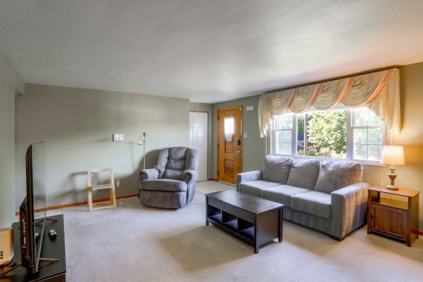 A living room with a grey sofa, a wooden coffee table, a grey armchair, and a television stand.
