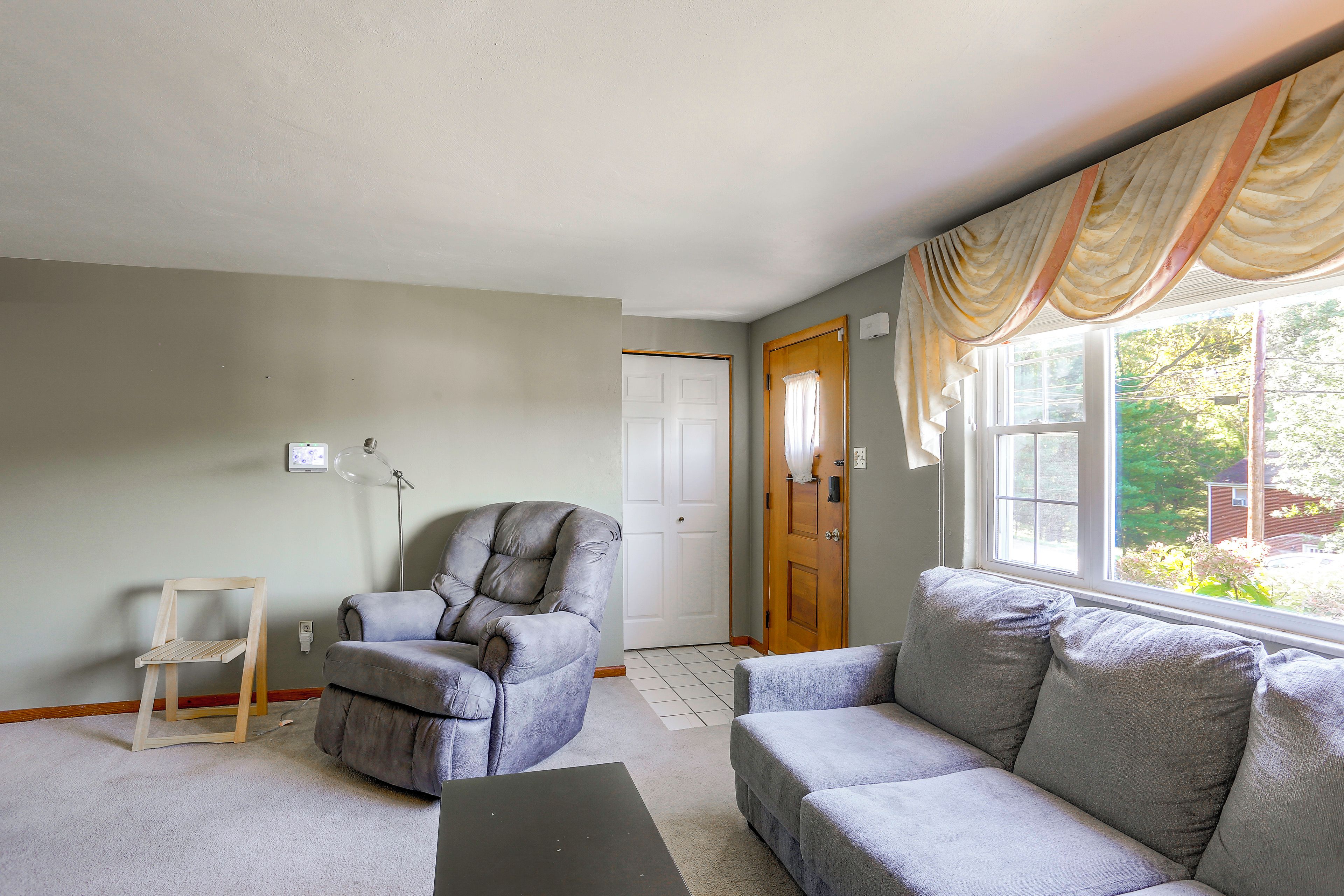 Una sala de estar con un sofá gris, una silla de madera, una lámpara y una puerta que da a otra habitación.