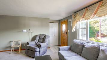 Una sala de estar con un sofá gris, una silla de madera, una lámpara y una puerta que da a otra habitación.