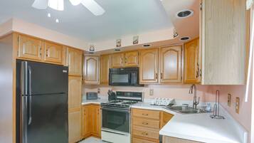 Una cocina con gabinetes de madera, un refrigerador negro, un microondas, una estufa y un lavamanos.