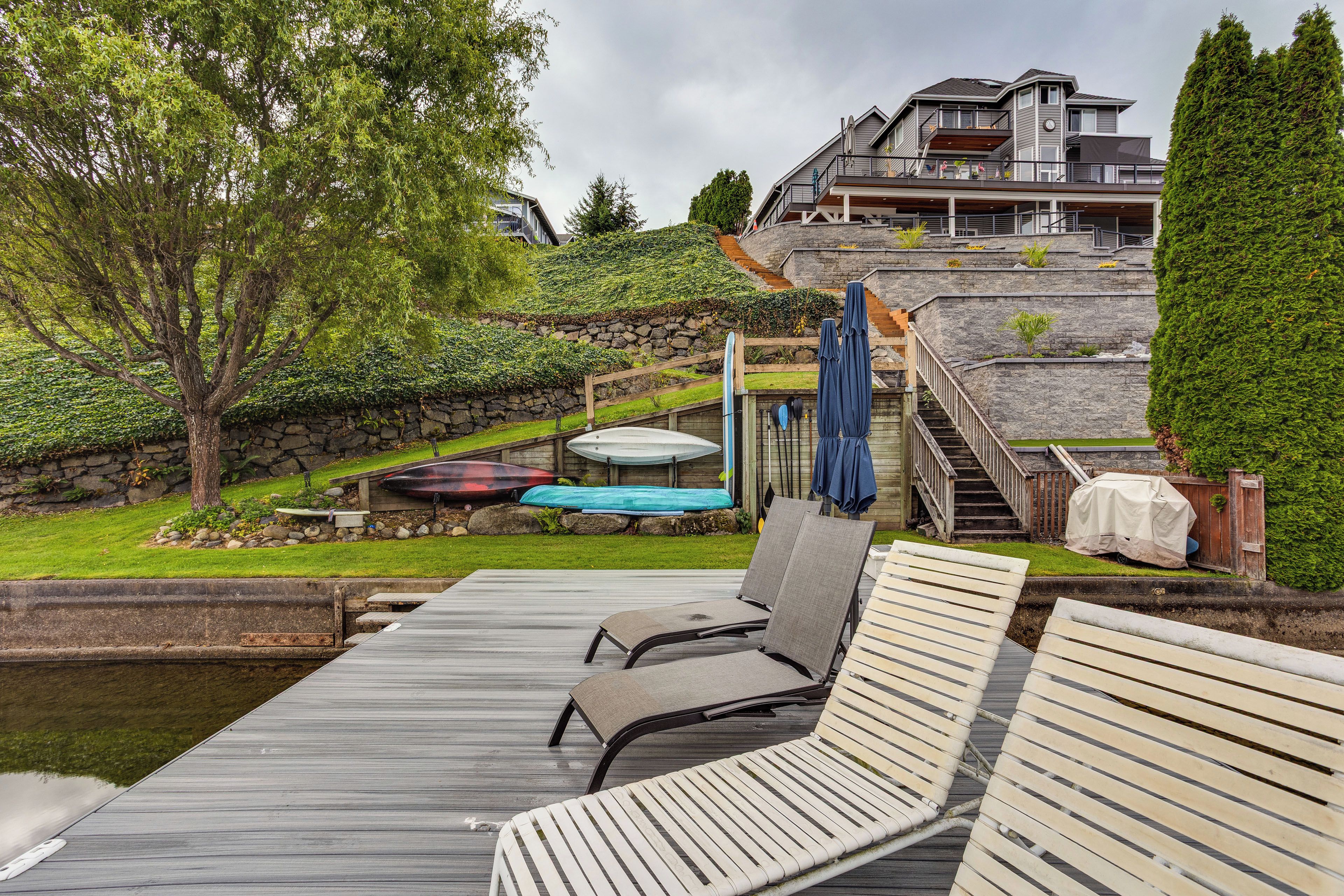 A deck with lounge chairs, a pool, and a stone wall with a staircase leading to a house.