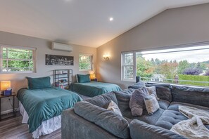 Ein Schlafzimmer mit zwei Betten, einem Sofa und einem großen Fenster mit Blick auf Bäume.