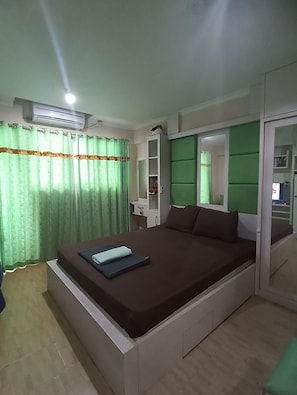 A bedroom with a bed, a wardrobe, a mirror, and an air conditioning unit. - THE ROOMOS Hotel Apartemen (Jakarta Timur)