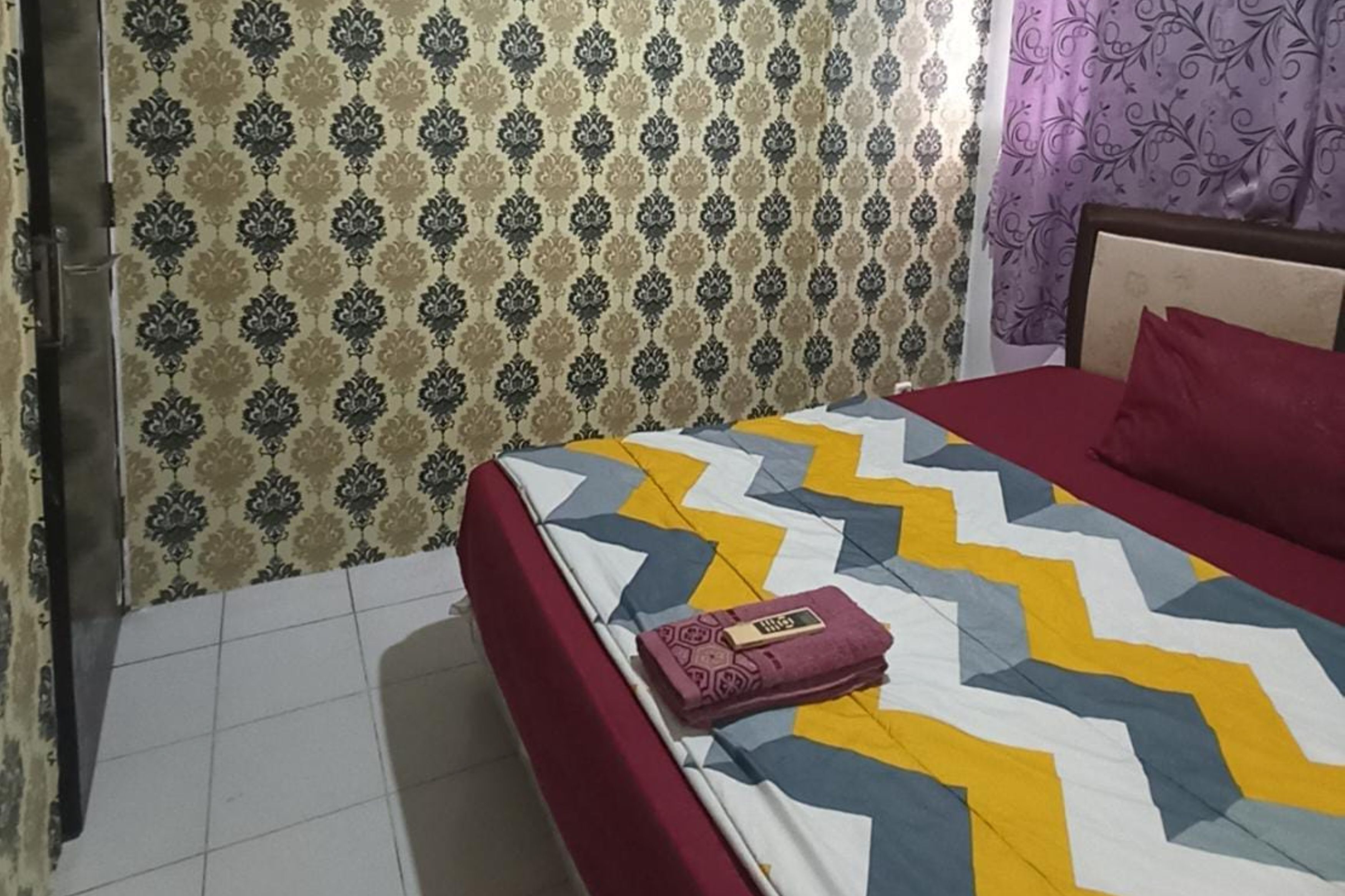 Una camera da letto con un letto, una testiera rossa, un muro decorato e una finestra con tende.