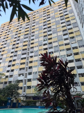 A high-rise building with multiple balconies and a swimming pool in the foreground. - THE ROOMOS Hotel Apartemen (Jakarta Timur)