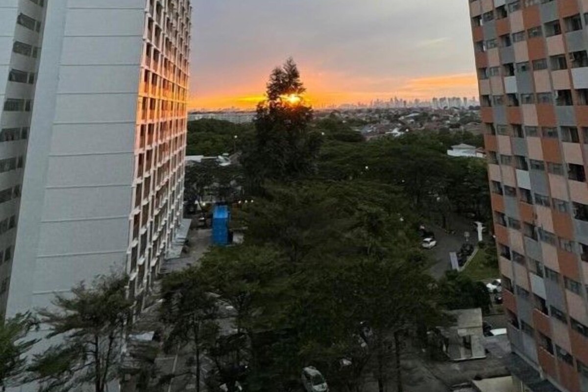 A high-rise building with a view of a sunset and a parking area with several cars.