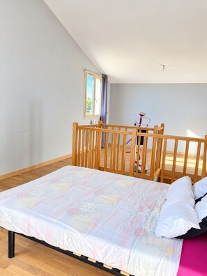 Ein Schlafzimmer mit einem Bett, einem Holz-Kinderbett und einem Fenster mit Vorhängen.