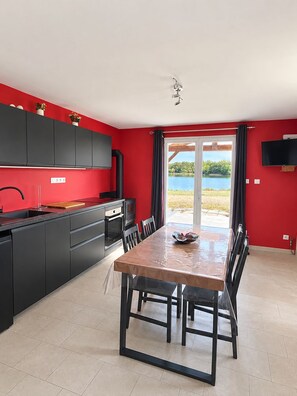 A modern kitchen with black cabinets, a dining table, and a view of a lake through a glass door.