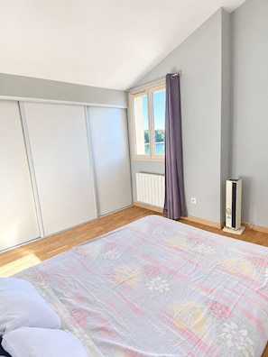 Un dormitorio con una cama grande, un radiador, una ventana con cortinas y un calentador portátil.