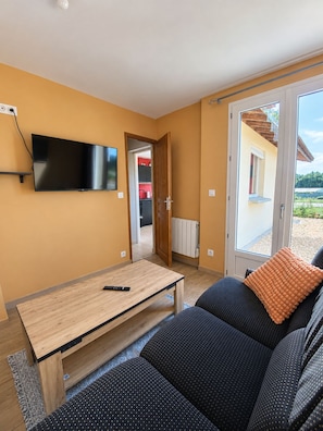 Ein Wohnzimmer mit einer Couch, einem Couchtisch, einem an der Wand befestigten Flachbildfernseher und einer Glastür, die zu einem Außenbereich führt.