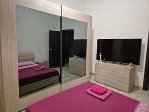 Una camera da letto con un letto, una cassettiera, uno specchio e un televisore.