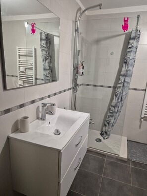 Un bagno con lavandino, specchio e doccia bianchi.