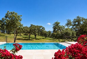 A rectangular swimming pool with clear blue water, surrounded by a tiled deck, and a view of a hilly landscape with trees and a clear sky. - Cubo's Villa La Caldera / private pool / gym / vineyards / luxury experiences / free Wi-Fi (Ronda)