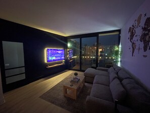 A modern living room with a large flat-screen TV, a sofa, a coffee table, and a large window offering a city view. - Luxury 2BR/2BA Tampa Channelside Downtown - Gym + Sauna + Pool  (Tampa)