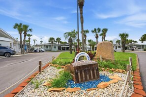 A beachfront property with a paved walkway, palm trees, and a sign indicating a beachside location. - PCB Getaway Resort Amenities Golf Cart Pools (Panama City Beach)