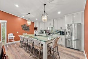 A modern kitchen with white cabinets, a stainless steel refrigerator, and a glass-top dining table with wicker chairs. - PCB Getaway Resort Amenities Golf Cart Pools (Panama City Beach)
