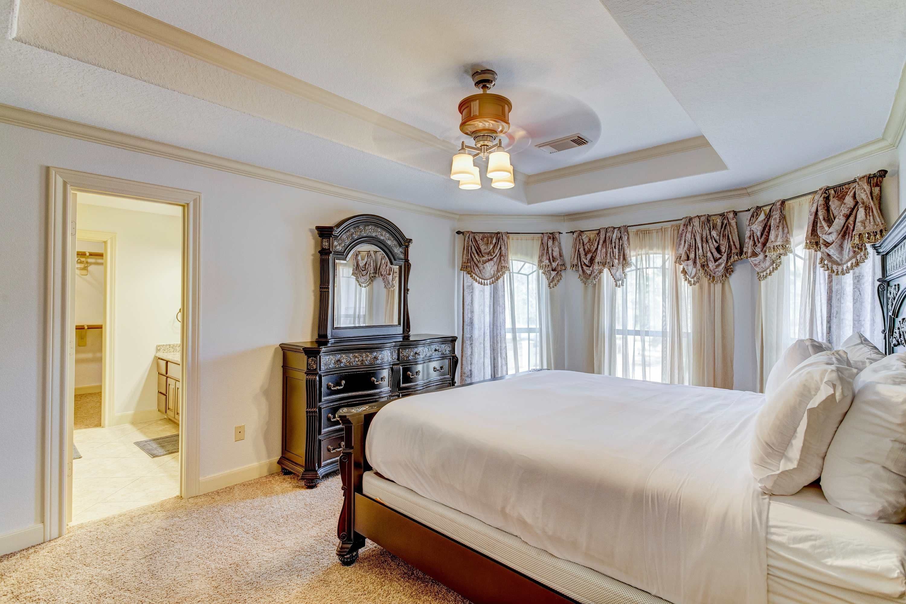A bedroom with a large bed, a dresser, a mirror, and a ceiling fan.