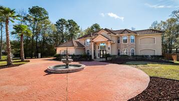A large two-story house with a landscaped driveway and a fountain.