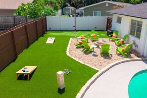 A backyard with artificial grass, a wooden table, green chairs, and a fire pit. - Pool Hot Tub Putt Putt Game Room Karaoke (Largo)