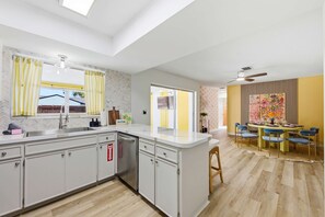 A modern kitchen with a central island, a dining area with a yellow table and blue chairs, and a ceiling fan. - Pool Hot Tub Putt Putt Game Room Karaoke (Largo)