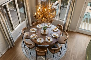 A round dining table with six chairs, a chandelier, and a view of the outdoors through large windows. - Starry Skies Sauna S Mores Pickleball Retreat (Blue Ridge)