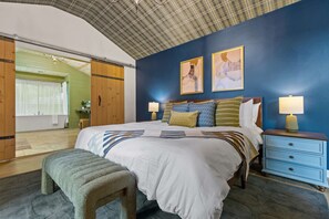 A bedroom with a large bed, two bedside lamps, a wooden bench, and a view of a bathroom. - Starry Skies Sauna S Mores Pickleball Retreat (Blue Ridge)