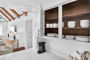 Cocina moderna con muebles blancos, una cafetera y un comedor con una mesa y sillas blancas.