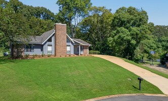 A two-story house with a brick chimney, surrounded by a well-maintained lawn and dense trees.