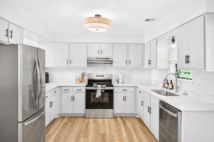 A modern kitchen with white cabinetry, stainless steel appliances, and a wooden floor.