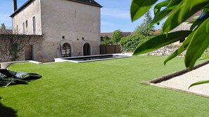 Ein gepflegter Rasen mit Pool, einer Steinmauer und einem Gebäude mit Bogenfenstern.