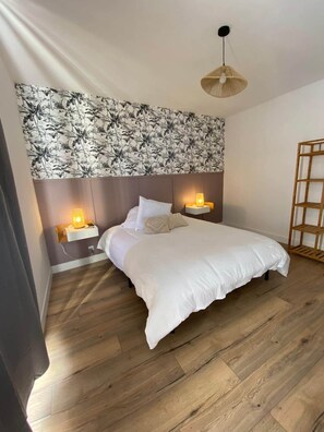 A bedroom with a bed, two bedside lamps, a wooden floor, and a wall with a tropical leaf pattern. - Group Home in Burgundy: L'antre amis (Molesme)
