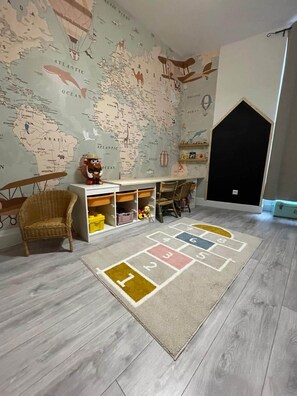 Ein Zimmer mit einer Weltkarte als Wandgemälde, einem Spielbereich mit einer Hula-Hoop-Bahn und einem Korbstuhl.