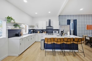 Een moderne keuken met witte kasten, een centraal eiland met barkrukken, een magnetron en een gasfornuis.