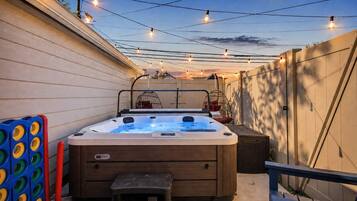 A hot tub with a wooden exterior, a bench, and a small table in a backyard setting.