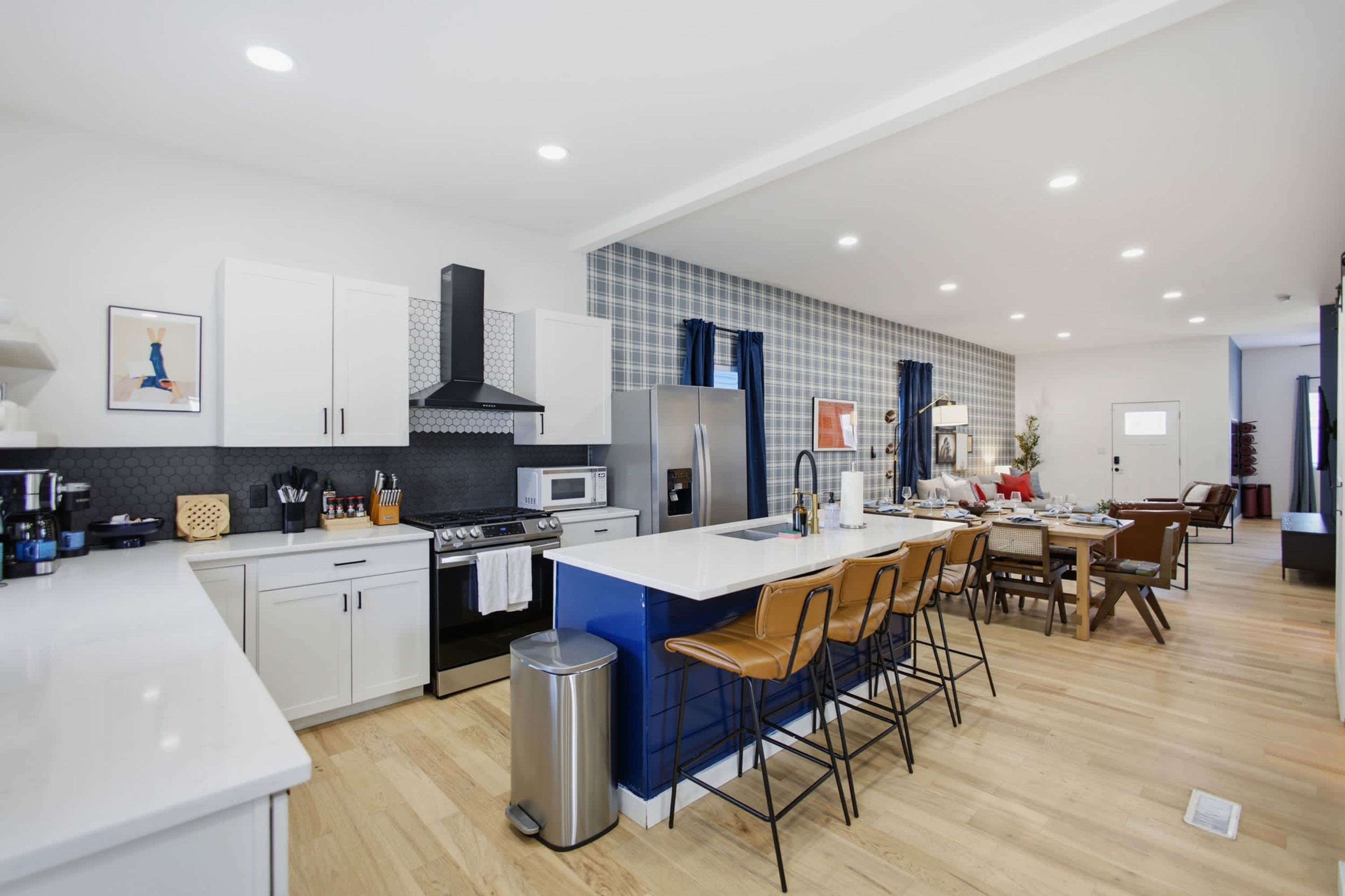A modern kitchen with white cabinets, a central island with bar stools, a black range hood, and a microwave.