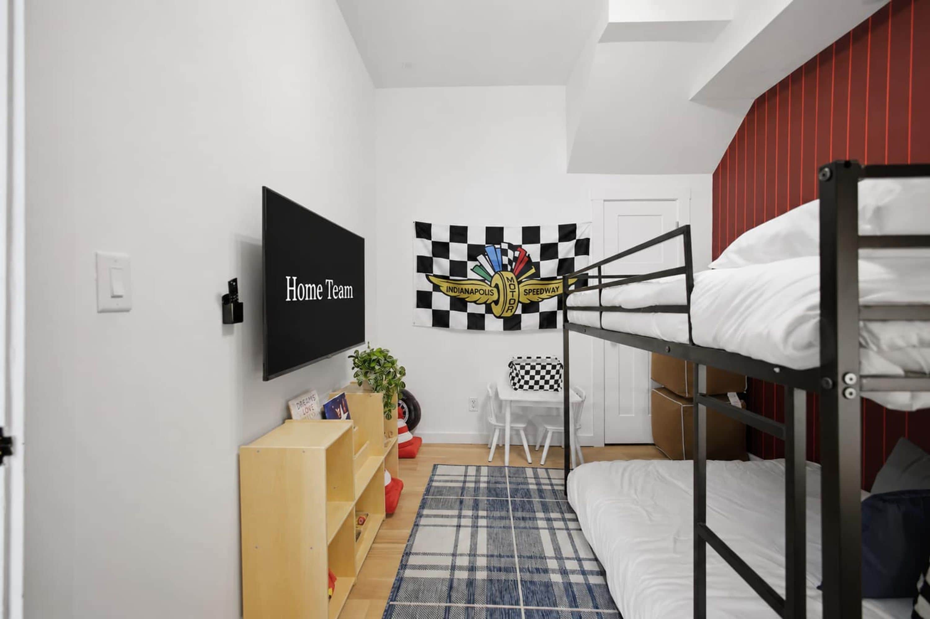 Una habitación con literas, televisión, decoración con bandera a cuadros, una mesita pequeña y una planta.