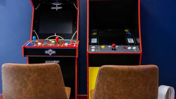 Deux bornes d’arcade, l’une portant l’inscription NBA JAM et l’autre Pac-Man, avec des chaises marron devant.