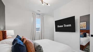 A hotel room with a bed, a flat-screen TV, a window with curtains, and a wall-mounted artwork.