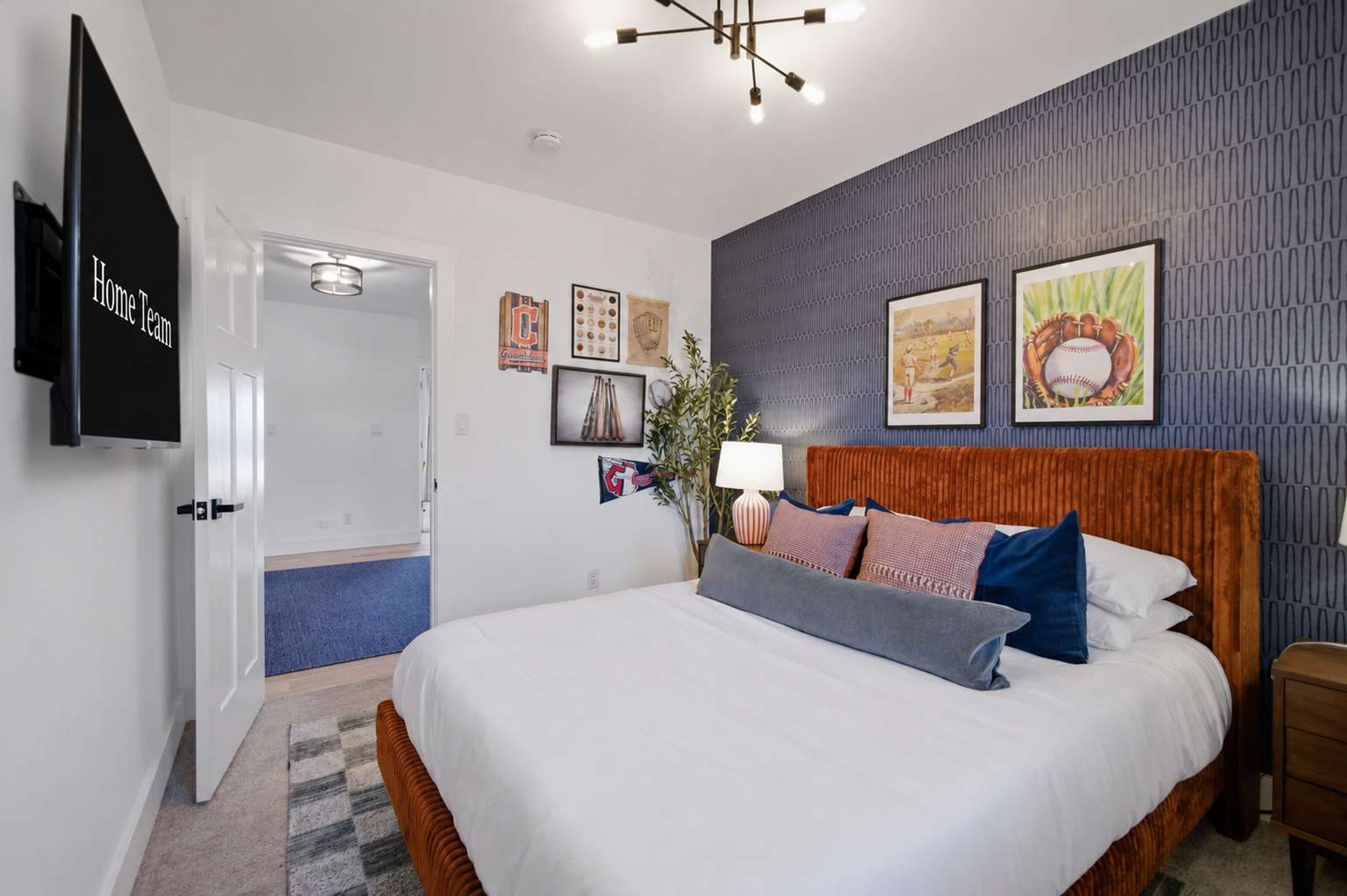 Une chambre d’hôtel avec un grand lit, un téléviseur à écran plat et un mur orné de souvenirs sportifs encadrés.