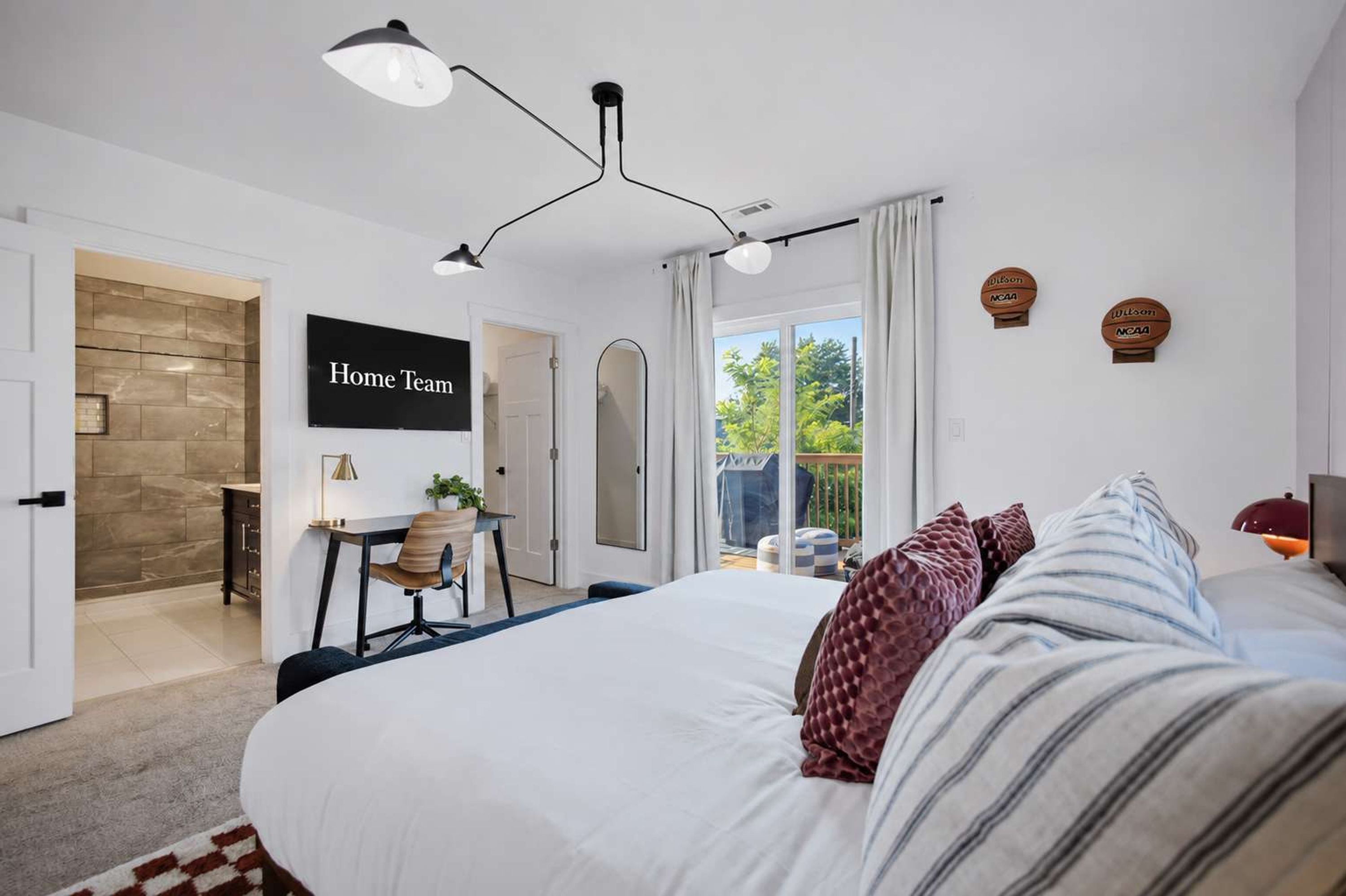 A modern bedroom with a large bed, a desk, and a view of the outdoors.