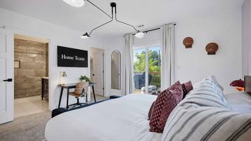 A modern bedroom with a large bed, a desk, and a view of the outdoors.