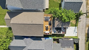 An aerial view of a residential area with multiple houses, a rooftop deck with outdoor furniture, and a small garden area.