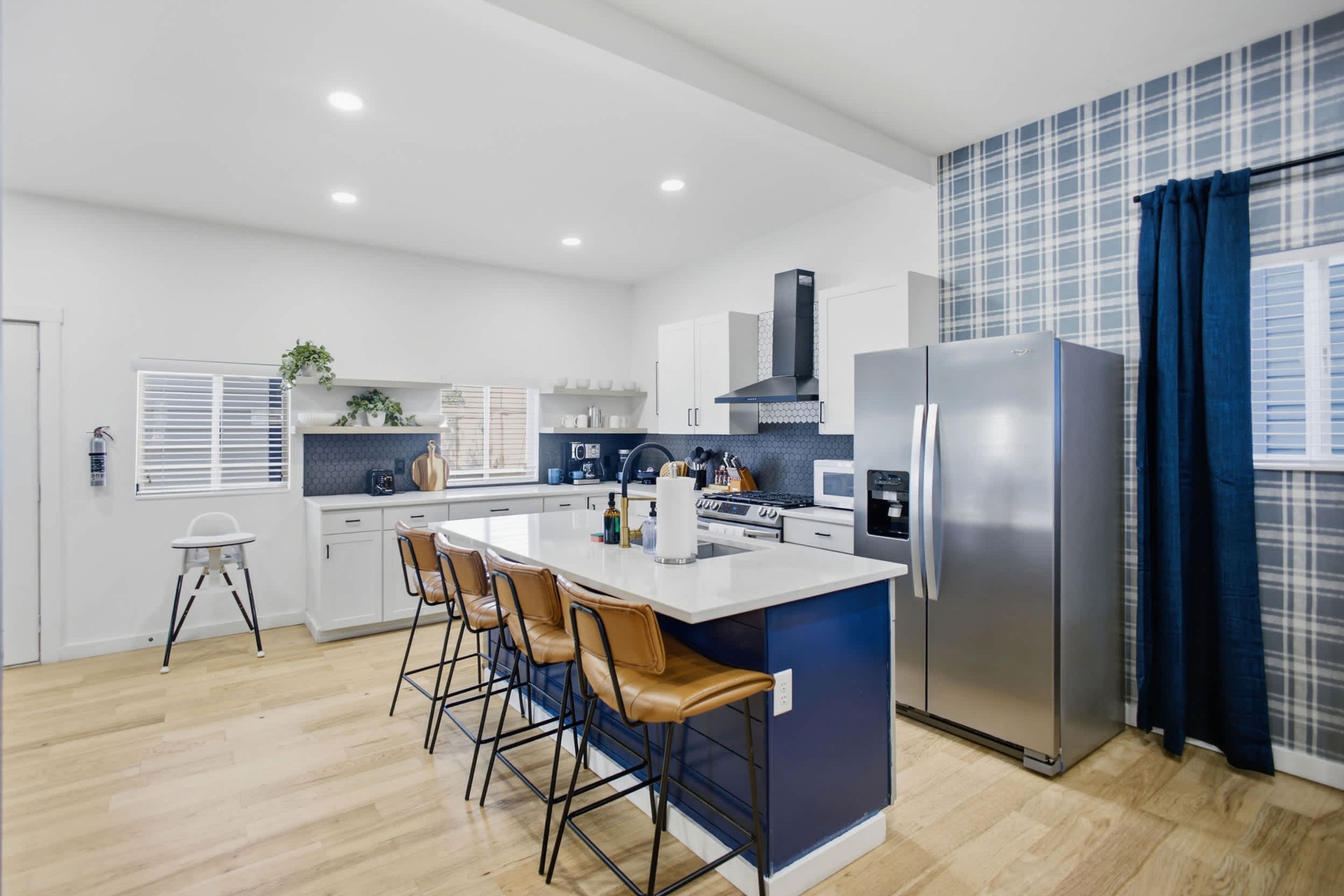 Une cuisine moderne dotée d’un îlot central, de tabourets de bar, d’un réfrigérateur en acier inoxydable et d’un mur d’accent bleu.