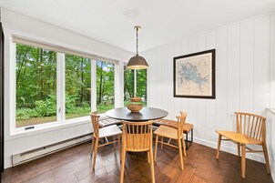 Un comedor con una mesa redonda, sillas de madera, una lámpara colgante y un ventanal con vistas a zonas verdes.