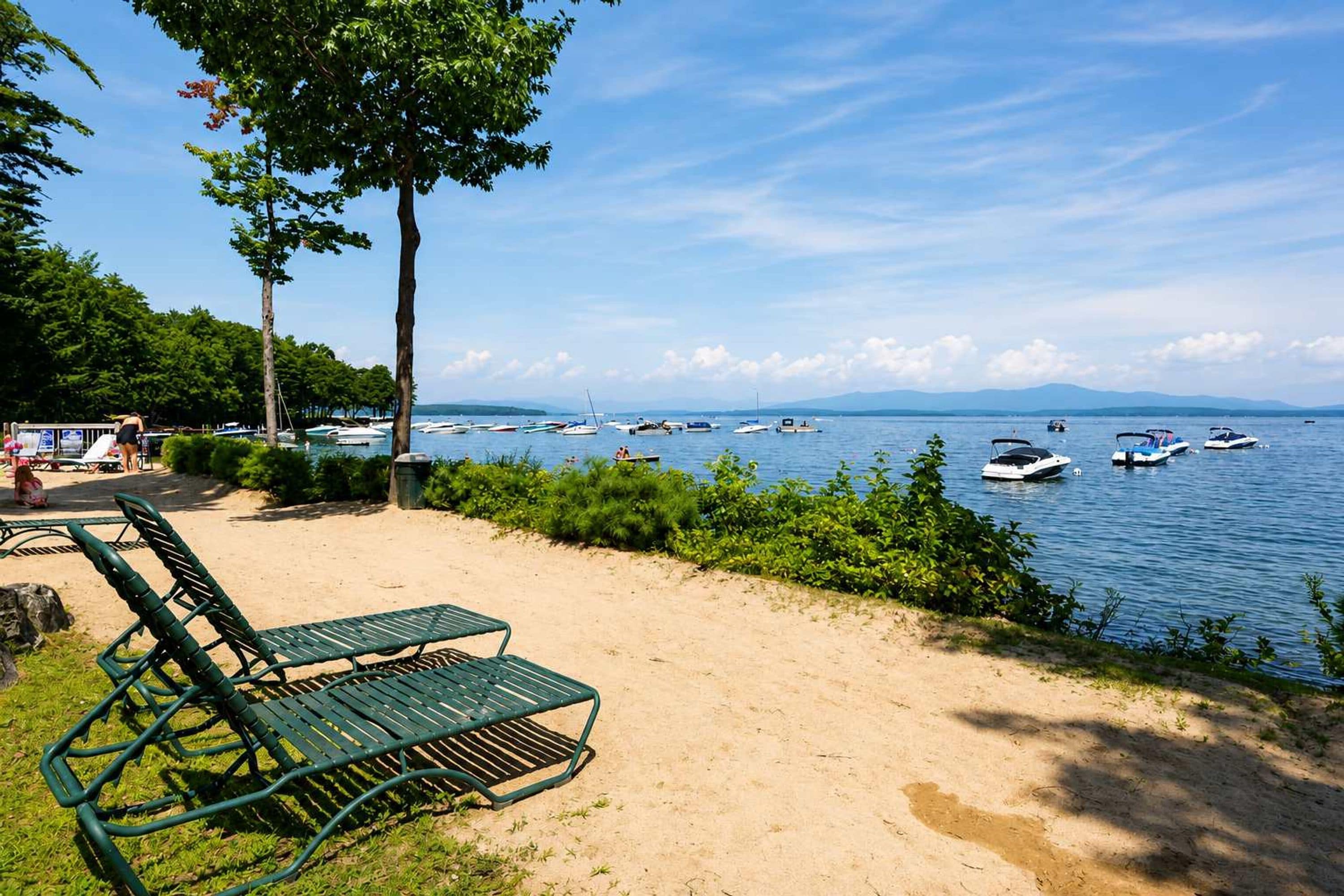 A beach with lounge chairs, a sandy area, and boats on the water.