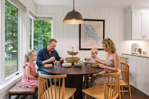 Una familia cenando en una mesa redonda con un mapa en la pared, sillas de madera y una lámpara colgante.
