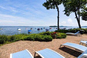 A waterfront patio with lounge chairs, a brick walkway, and boats on the water.